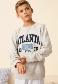 Jasnoszary sweter z okrągłym dekoltem, długimi rękawami oraz niebieskim napisem "ATLANTA TRACK & FIELD 1976" na przodzie. Wykonany z materiału z domieszką bawełny.
