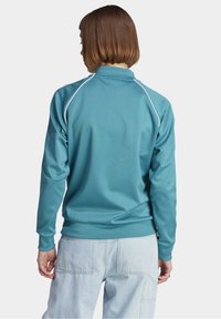 Tyrkysová mikina s vysokým límcem a bílým lemem podél ramen. Měkká tkanina se volným střihem, doplněná o světle modré cargo kalhoty.