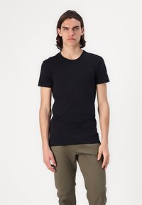 T-shirt en coton noir avec un col rond et des manches courtes, associé à un pantalon vert olive. Design simple et ajusté, sans motifs ni graphiques visibles.
