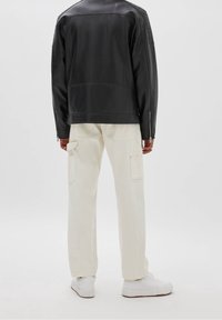 Veste en cuir noir au design structuré, associée à un pantalon cargo blanc cassé avec poches latérales et des baskets blanches.