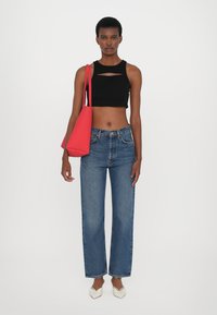 Top noir courts avec une découpe, jean droit bleu, chaussures blanches à bout pointu, et un sac à épaule rouge, sur fond blanc uni.