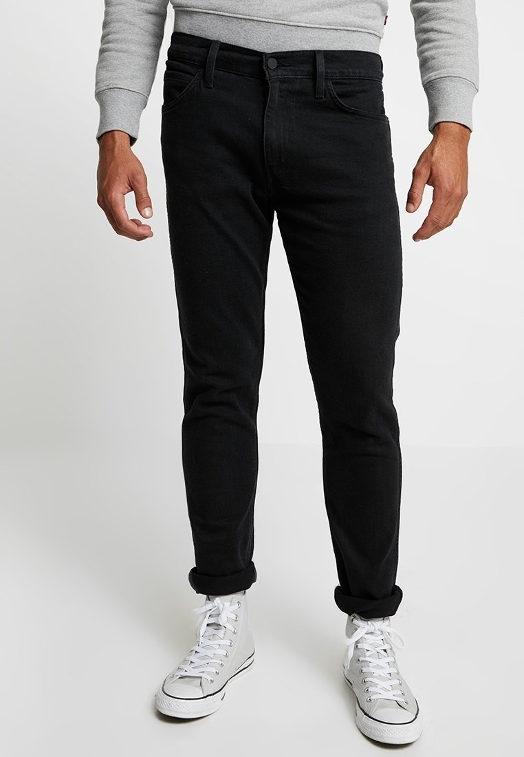 Jeans in denim nero slim fit, con un classico design a cinque tasche, orli arrotolati, indossati con sneakers bianche alte.