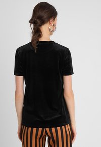 Svart sammets t-shirt med korta ärmar, rundad halsringning och en mjuk yta. Designen har en figurnära silhuett.