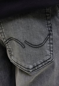 Baklomme på grå denimjeans med svart, buet søm, brukt med en svart topp.