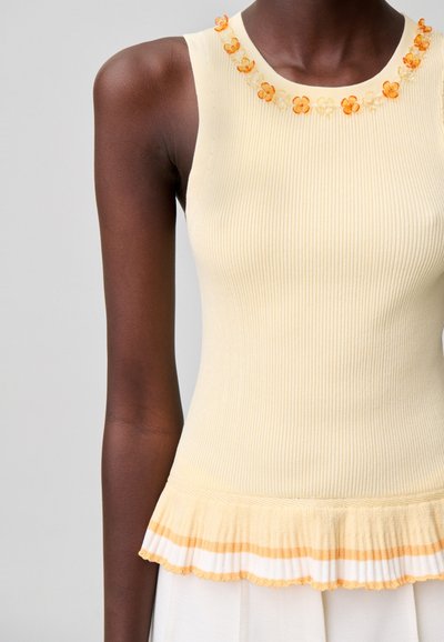 Top sin mangas en crema con textura acanalada, adornos de flores naranjas en el escote y bajo fruncido con rayas blancas y naranjas.