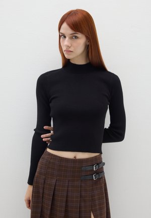 Haut noir à manches longues côtelé avec un col montant associé à une jupe à carreaux marron avec des boucles et une fente sur le côté. Texture lisse, design ajusté.