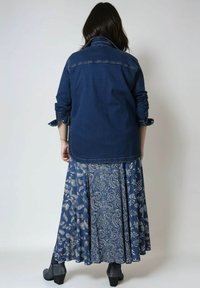 Denim jacket in dark blue with a collared neck and rolled sleeves, paired with a long, patterned blue skirt featuring white floral motifs.