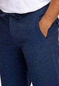 Mörkblå linnebyxor med en avslappnad passform, som har framfickor och resårmed dragsko i midjan. Tyget har en strukturerad, mjuk yta.