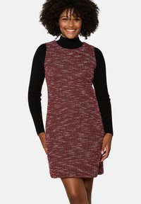 Vestido rojo texturizado con un diseño sin mangas, que presenta un cuello alto negro debajo. Las costuras visibles y las aberturas en los laterales realzan su diseño.