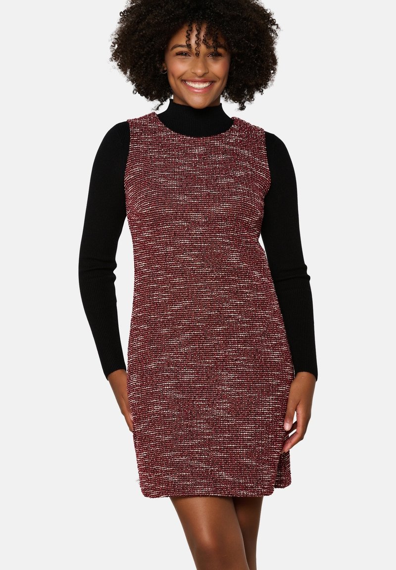 Vestido rojo texturizado con un diseño sin mangas, que presenta un cuello alto negro debajo. Las costuras visibles y las aberturas en los laterales realzan su diseño.