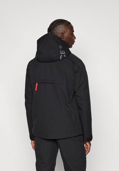 Čierna nepremokavá bunda s kapucňou, s logom na chrbte, červeným detailom na vrecku a textúrovanou látkou pre zvýšenú odolnosť.