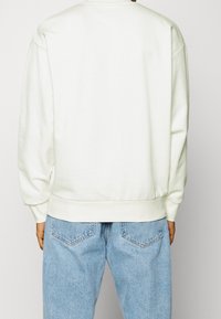 Sweat-shirt blanc avec ourlet et poignets côtelés, associé à un jean en denim bleu clair présentant une conception classique à cinq poches et des coutures visibles.