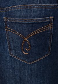 Un tissu en denim bleu foncé présente une poche arrière avec une couture dorée-brun complexe formant un motif stylisé sur le dessus.