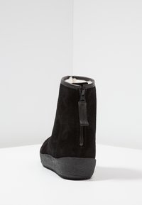 Bottine en suédine noire avec une semelle en caoutchouc texturé, fermeture éclair et doublure douce. Bout rond et design minimaliste.