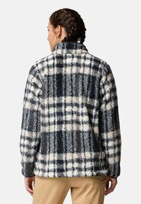 Giacca in pile con motivo a scacchi nero, bianco e grigio; colletto alto, maniche lunghe e tasche laterali. Tessuto morbido e vestibilità rilassata.