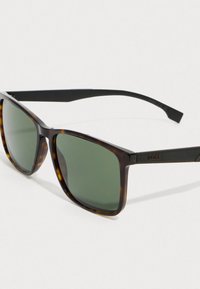 Aurinkolasit, joissa on kilpikonnakuosiset neliökehykset, vihreät linssit ja mustat varret, joissa on huomaamaton "BOSS" -merkintä sivussa.