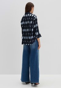 Zwarte en blauwe geblokte blouse met een knoopsluiting en driekwart mouwen, gecombineerd met brede denim broek. Soepele stofstructuur.
