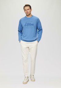 Felpa azzurro chiaro con stampa scura, abbinata a pantaloni color crema e sneakers basse con accenti grigi e beige.