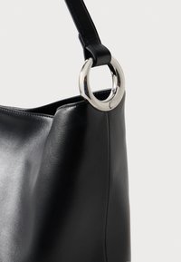 Bolso de mano negro de cuero con textura suave, con un acento de metal plateado redondo en la correa. Diseño simple y forma curva.