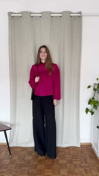 Blusa fúcsia com mangas bufantes e decote rendado, combinada com calças pretas de perna larga. Uma pequena bolsa preta é usada ao ombro.
