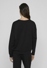 Juodas, ilgos rankovės džemperis su laisvu kirpimu, nuleistais pečiais ir raukšlėtais rankogaliais. Lygus paviršius, paprastas dizainas be matomų raštų.