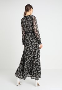 Czarna długa sukienka w kwiaty z przezroczystymi długimi rękawami, dopasowanym w pasie i zwiewnym dołem. Posiada czarny pasek w talii i jasne kwiatowe wzory.