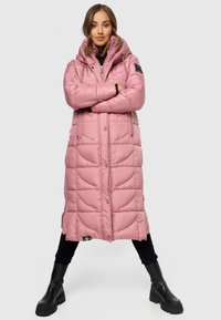 Long pink puffer coat with a hood, featuring a quilted design and front button closure, paired with black ankle boots.