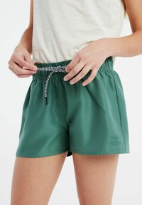 Shorts verts en tissu lisse, dotés d'une taille élastique avec un cordon noir et blanc et d'un petit logo sur le côté.