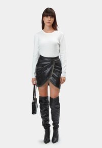 Maglione bianco lavorato a maglia, gonna avvolgente in pelle nera con dettagli frangi, stivali neri fino al ginocchio e una piccola borsa nera.