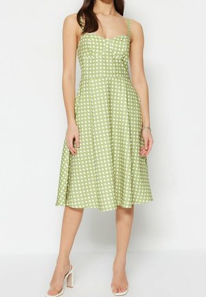Groene midi-jurk met een nauwsluitend lijfje en een uitlopende rok. Voorzien van witte geometrische patronen en dunne spaghettibandjes. Soepele stoftextuur.