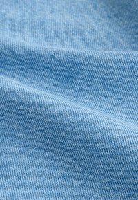 Tissu en jean bleu clair avec une finition texturée, affichant un motif de tissage diagonal et des fils fins, plié pour montrer la profondeur et la texture.