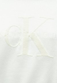Weißer Strickpullover mit einem plüschigen, erhabenen "CK"-Logo in Creme. Glatte Textur mit detaillierter Nahtarbeit und subtiler Markenkennzeichnung.