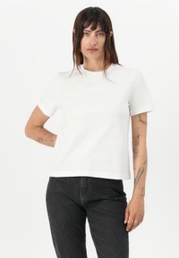 Witte katoenen t-shirt met korte mouwen en een ronde hals. Heeft een subtiele logo gecentreerd op de borst. Gecombineerd met donkere jeans.