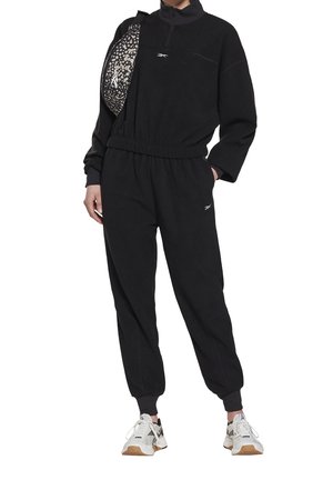 Černá fleecová tepláková souprava se zipovým límcem, elastickým pasem a manžetami u kotníků, doplněná vzorovanou crossbody taškou a teniskami.