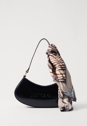Czarna, zakrzywiona torebka z tłoczonym logo "JUST CAVALLI" oraz beżowym, wzorzystym szalikiem przywiązanym do uchwytu, na gładkim tle.