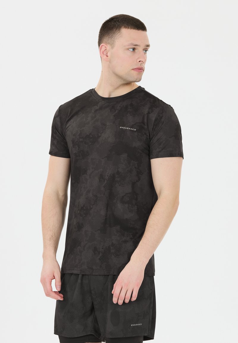 Musta urheilupaita lyhyillä hihoilla, jossa on teksturoitu maastokuvio ja sana "KESTÄVYYS" painettuna vasemmassa rintaosassa.