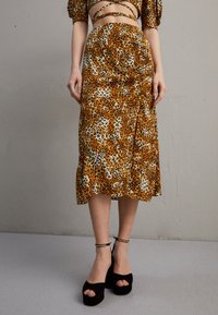 Leopardenmuster Midirock mit einer seidigen Textur in orange, schwarz und cremefarben, kombiniert mit schwarzen Plateausandalen mit offenen Zehen und Knöchelriemen.