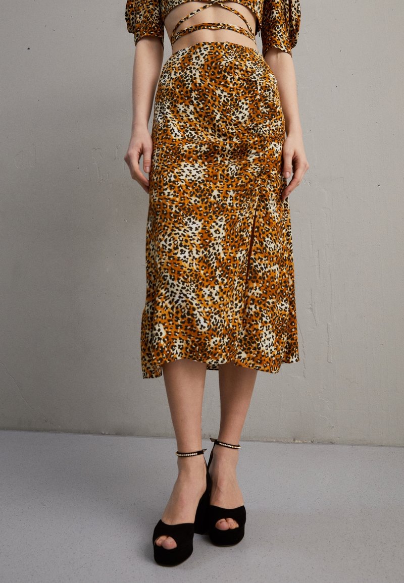 Leopardenmuster Midirock mit einer seidigen Textur in orange, schwarz und cremefarben, kombiniert mit schwarzen Plateausandalen mit offenen Zehen und Knöchelriemen.