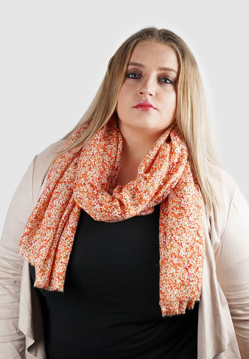 Sinaasappel- en roomkleurige sjaal met bloemenpatroon, gemaakt van lichtgewicht stof, losjes om de nek gedrapeerd, met rafelige randen en een zachte textuur.