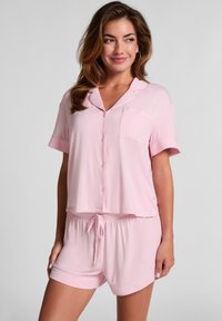 Lichtroze pyjama set met een kortgebreide, knoopsluiting bovenkant met een zak en shorts met een koord, gemaakt van een zachte stof met een gladde textuur.