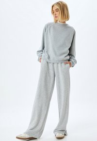 Lichtgrijze sweatshirt en wijde pantalons gemaakt van zachte stof. Heeft een relaxte fit, geribbelde manchetten en zijzakken. Geaccentueerd met een ronde hals.