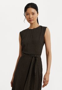 Black dress with short sleeves, featuring a textured pattern of small dots in gold. It has a fitted waist with a tie detail.