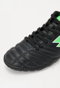 Black soccer shoe with textured leather, featuring black laces and vibrant green accents. The design includes stitched detailing on the upper.