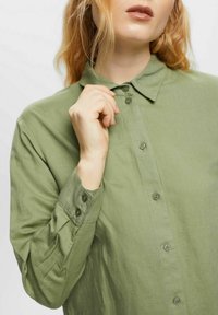 Camicia verde chiaro con colletto a punta, texture morbida e maniche lunghe con polsini abbottonati. Design semplice e pulito.