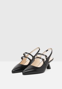 Tacchi slingback in pelle nera con punta appuntita, caratterizzati da due cinture incrociate e fibbie argentate, posti su un tacco basso a blocco.