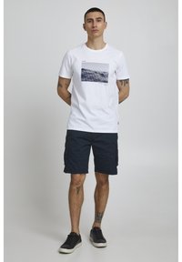 Vit bomulls t-shirt med ett blått grafiskt tryck på framsidan, matchad med marinblå cargoshorts och svarta sneakers. Enkelt, avslappnat design.