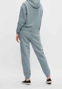 Felpa grigia chiara e pantaloni jogger abbinati in morbido tessuto. L'outfit presenta un cappuccio e polsini elastici alle caviglie. Indossato con sneaker nere.