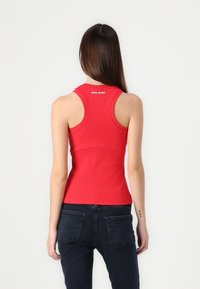 Tricou roșu cu dungi, cu un gât rotund și design racerback, având un logo pe spate, asortat cu blugi de culoare albastru închis.