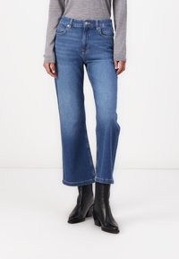 Kõrge vöökoht ja lõdva lõikega sinised denim püksid. Omavad viit taskut, diskreetset õmblust ja puhta servaga viimistlust. Kombineeritud mustade pahkluupükste kingadega.