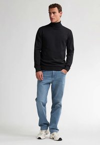 Maglione nero a collo alto, design aderente, polsini e orlo a coste, abbinato a jeans di denim azzurro chiaro e sneaker bianche. Abbigliamento semplice e casual.